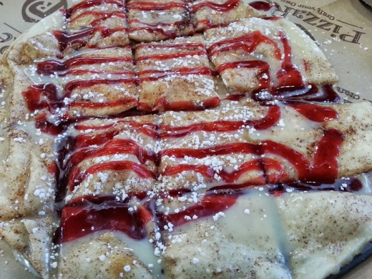 A sweet, tender dessert pizza topped with frosting and raspberry sauce.