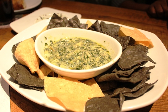 Spinach and artichoke dip with white and blue corn tortilla chips.